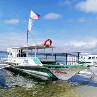 A white and green outrigger boat with a Philippine flag in clear water