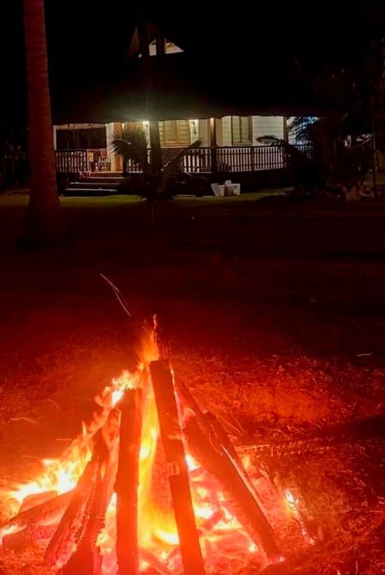 A bonfire blazing at night with the lit main building behind
