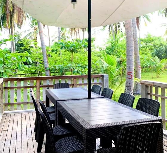 A long dark table and chairs on a timber deck overlooking greenery