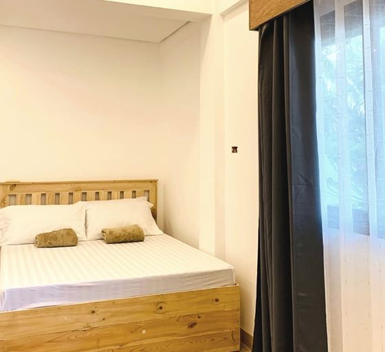 A timber double bed beside a window with sheer and grey curtains