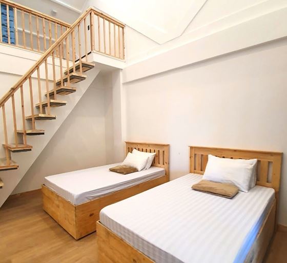 Two twin beds below a timber staircase to the loft