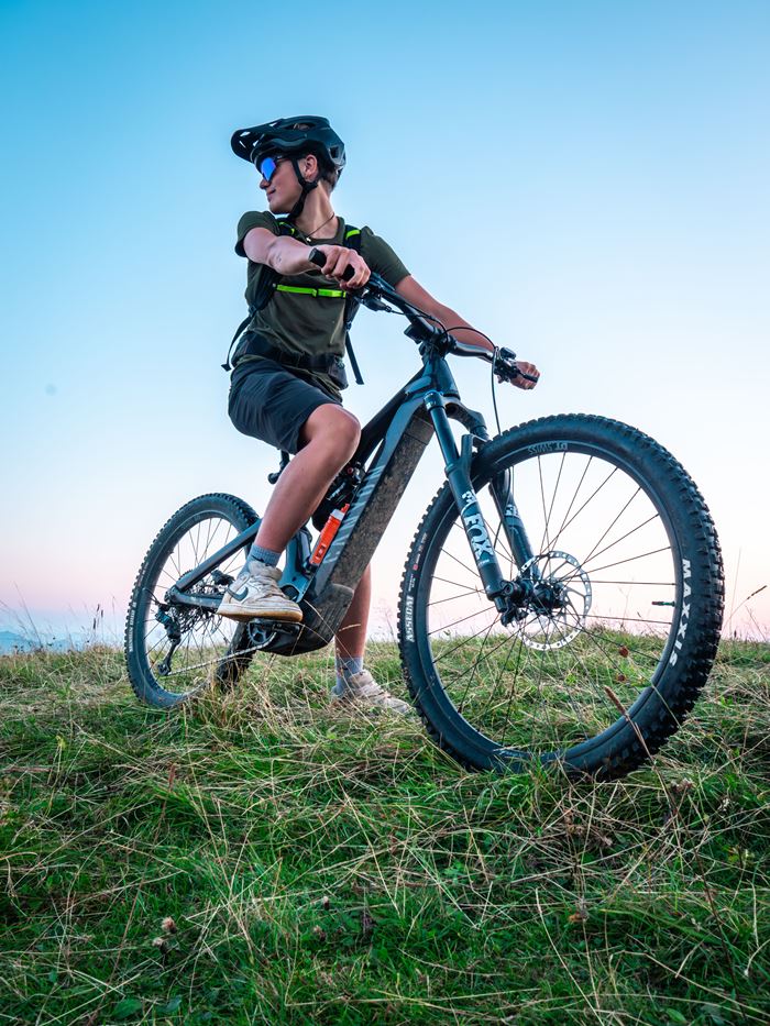 A cyclist in a helmet resting on a mountain bike on a grassy hilltop