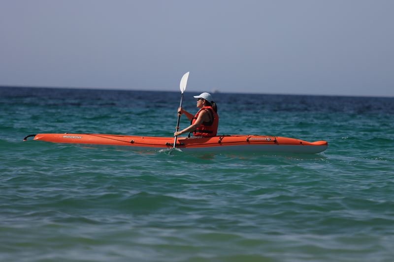 A paddler in an orange kayak on calm green sea water