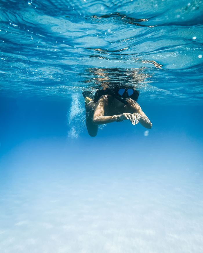 A snorkeller swimming underwater through clear blue water