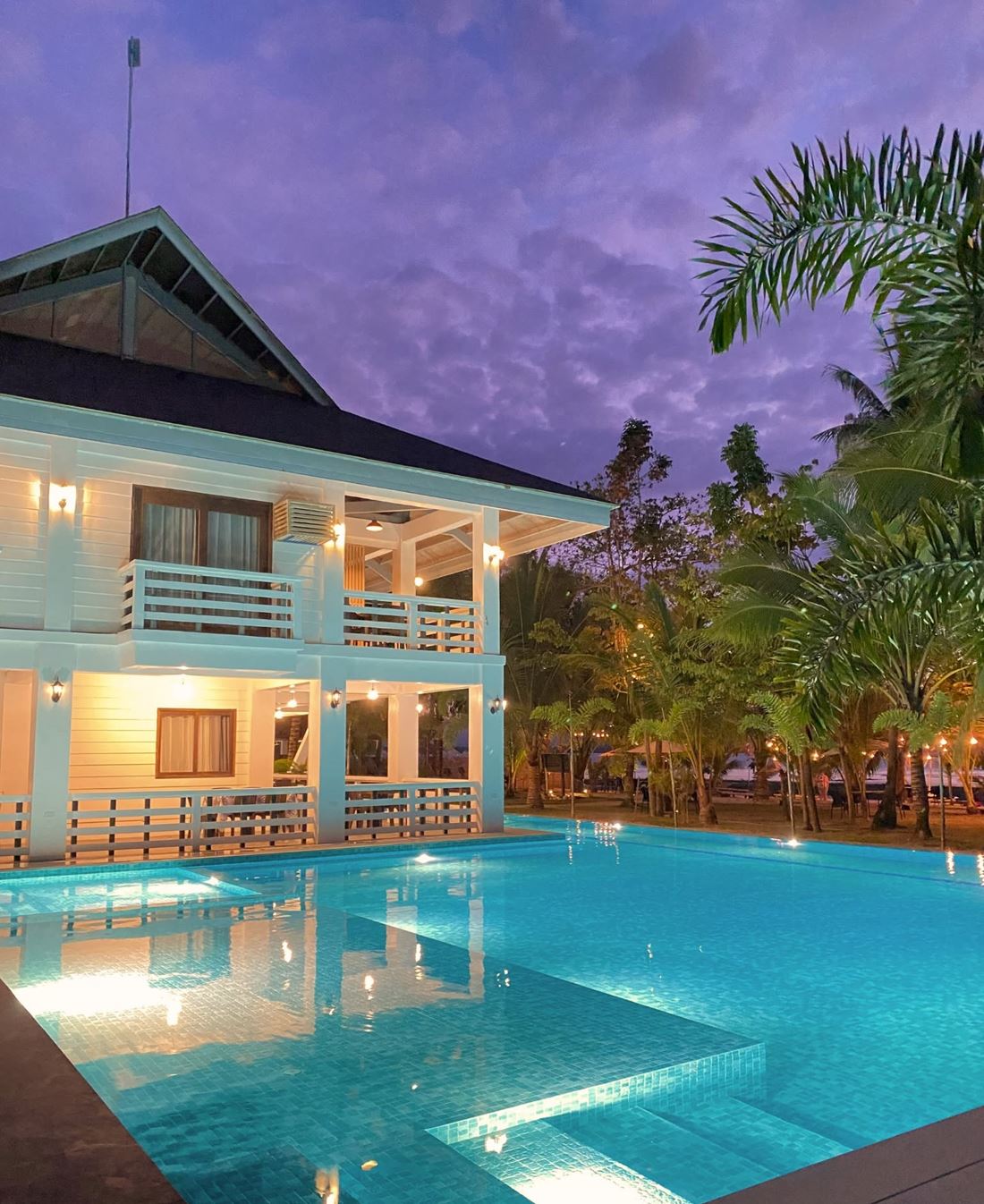 The resort's turquoise pool with its shallow sun shelf beside the main building, lit at dusk