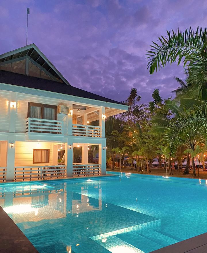 The main building lit at dusk beside the turquoise pool and palms