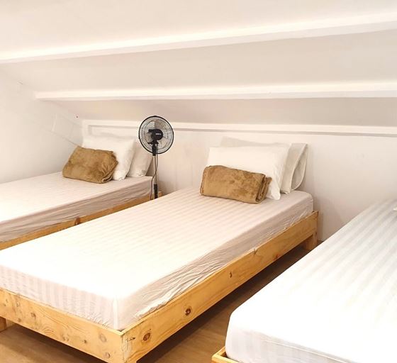 Three single beds with timber frames under a sloping white ceiling
