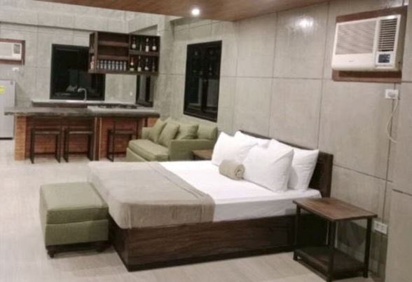 Inside the Pool Suite Room: a queen bed with a padded bench, a green sofa and a kitchen counter with bar stools