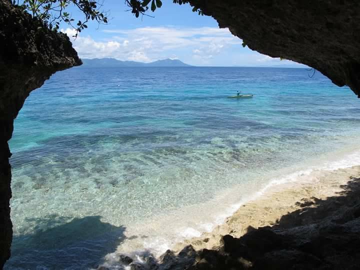 View of the turquoise bay and a small boat framed by a coastal rock arch near Padre Burgos