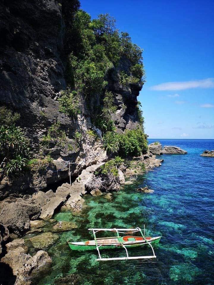An outrigger boat anchored below a cliff in clear turquoise water