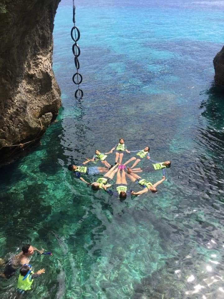 A group of guests linking hands in the water below a rope swing at a cliff cove