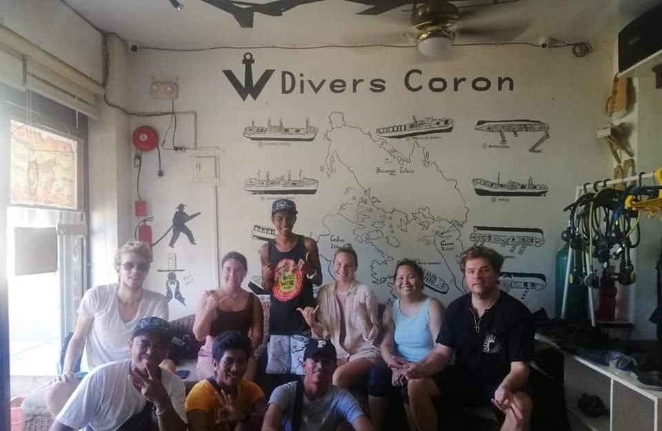 The W Divers Coron team and guests at the shop, in front of the dive-site map wall