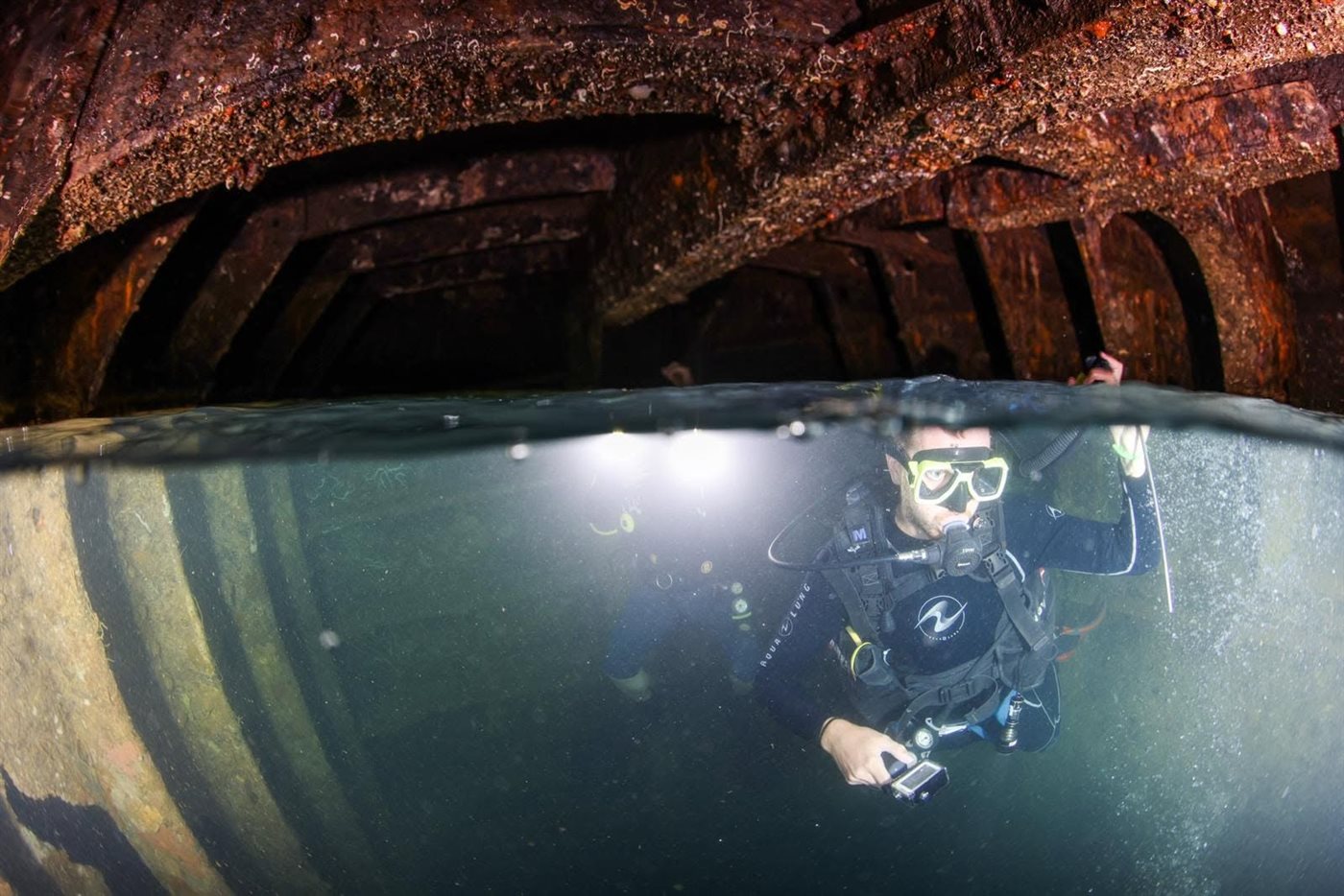 A diver surfacing inside the rusted hull of a WWII shipwreck in Coron Bay